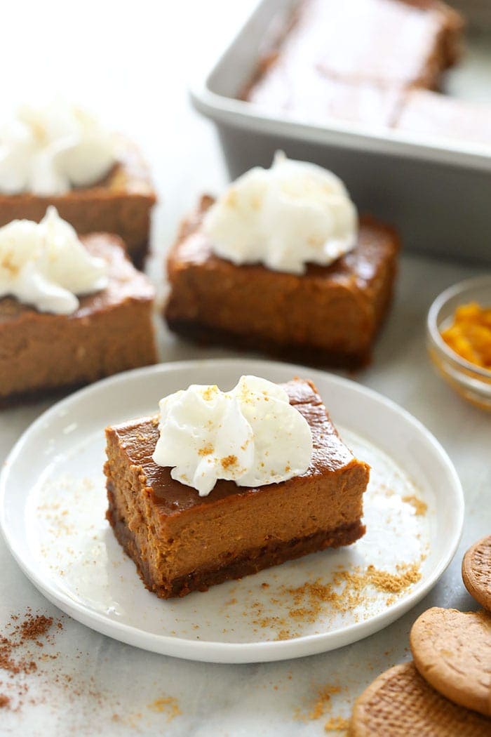 Say hello to the ultimate harvest dessert! These Pumpkin Cheesecake Bars with a gingersnap crust and a delicious pumpkin pie cheesecake filling are perfect for wowing your dinner guests, but easy enough for a simple night in. pumpkin cheesecake bar topped with whipped cream on a plate