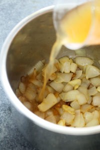 A liquid is being poured into a bowl of onions to make instant pot butternut squash soup.