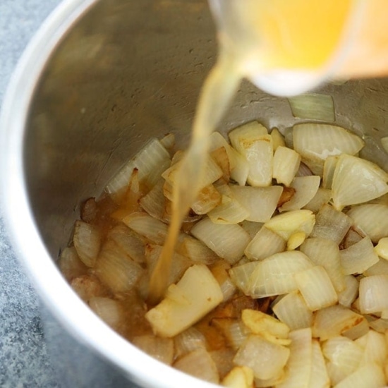 A liquid is being poured into a bowl of onions to make instant pot butternut squash soup.