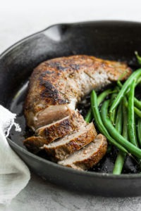 Sous vide pork tenderloin with green beans cooked in a skillet.