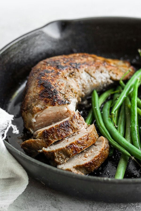 A sous vide pork tenderloin served with green beans in a skillet.