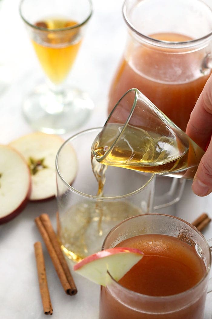 shot of booze being poured in a mug for spiked apple cider