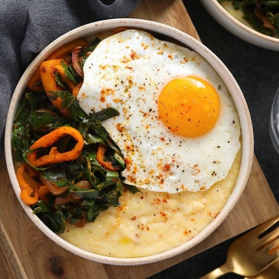 A bowl with cheesy grits topped with a fried egg and greens.