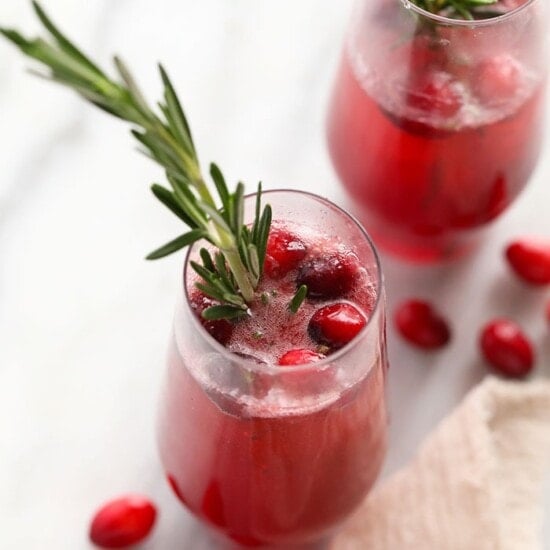 Two glasses with cranberries and rosemary sprigs.