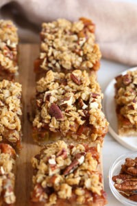 Apple crisp bars with granola and pecans, resembling apple pie bars, displayed on a cutting board.