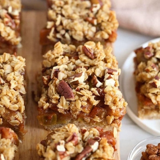 Apple crisp bars with granola and pecans, resembling apple pie bars, displayed on a cutting board.