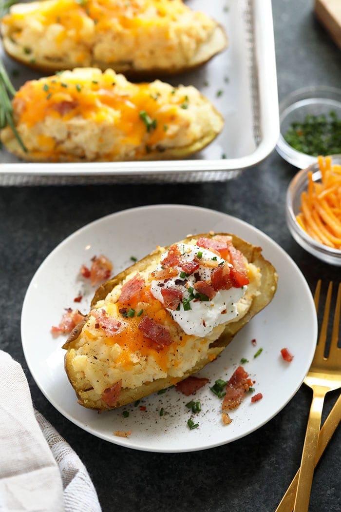 twice baked potato on a plate topped with bacon, chives and greek yogurt