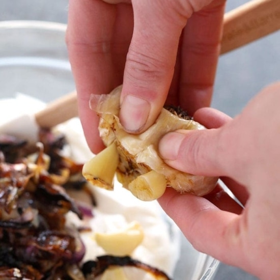A person preparing caramelized onion dip by slicing onions into a bowl.