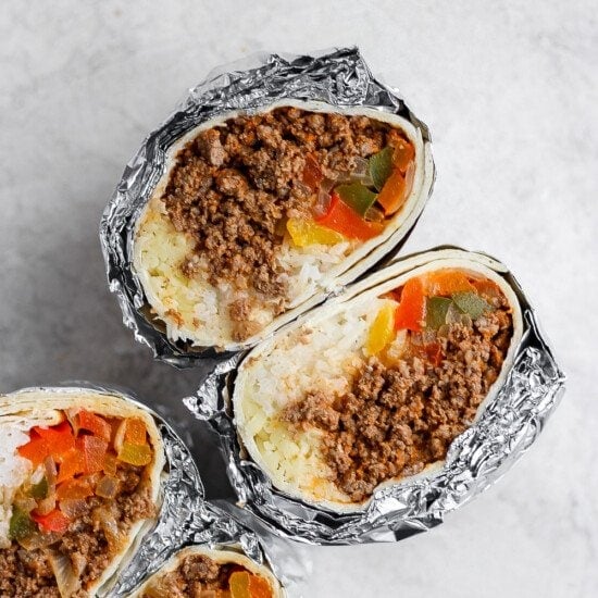 Three frozen burritos wrapped in foil with meat and vegetables.