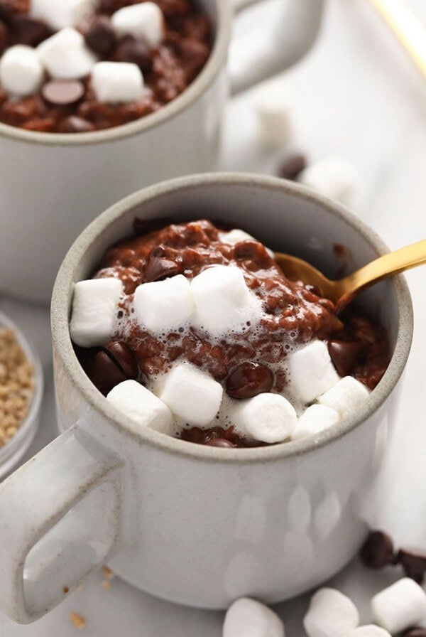 Two mugs of hot cocoa filled with chocolate and marshmallows.