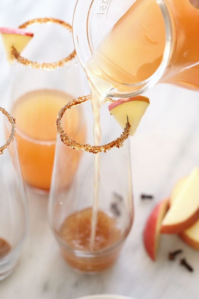 pouring an apple cider mimosa into a festive glass.
