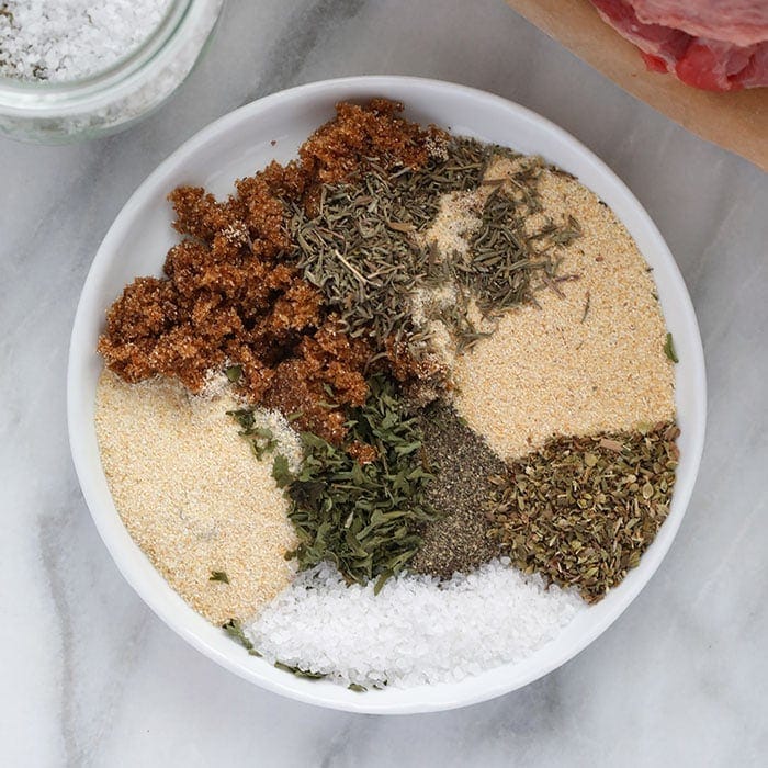 A jar of pot roast seasoning next to a bowl of spices and herbs.