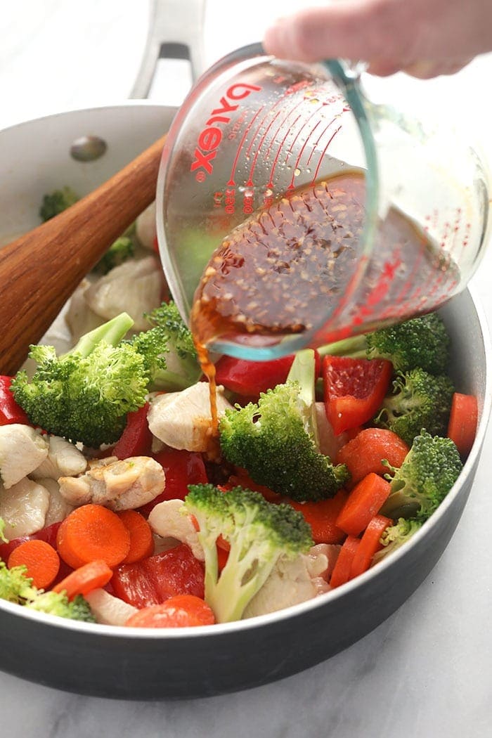 Pouring teriyaki sauce over chicken and vegetables