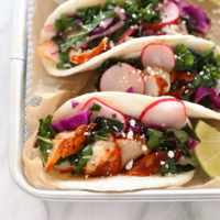 Three fish tacos with kale and radishes on a tray.