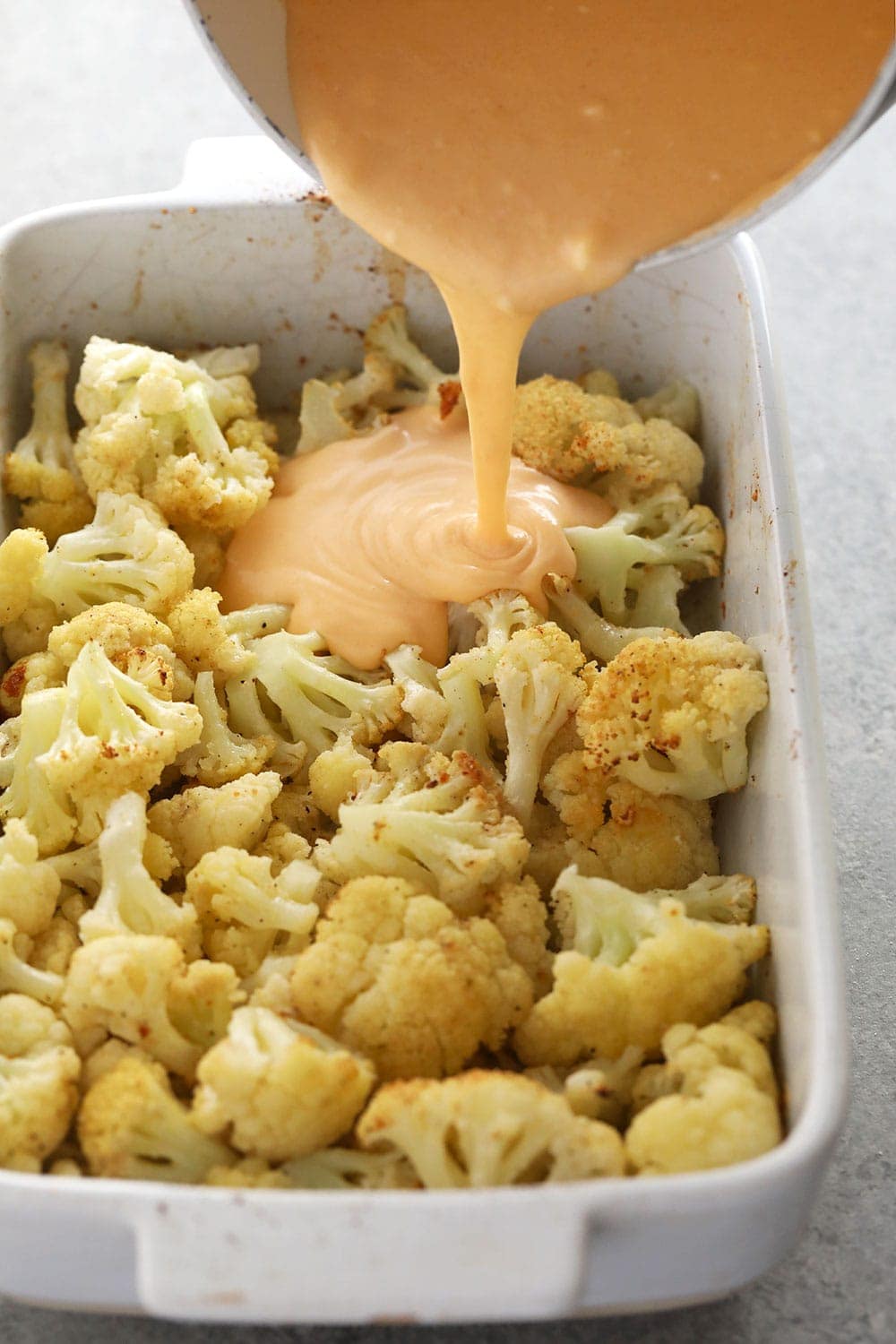 cauliflower mac and cheese with the sauce being poured over cauliflower