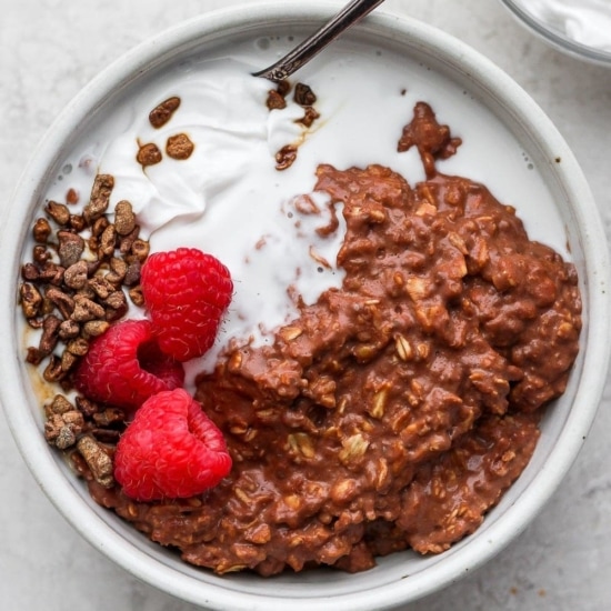 a bowl of oatmeal with chocolate granola, raspberries, and whipped cream.