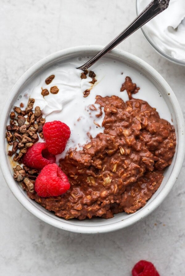 a bowl of oatmeal with chocolate granola, raspberries, and whipped cream.
