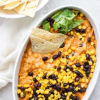Street corn and queso dip in a white bowl with black beans.