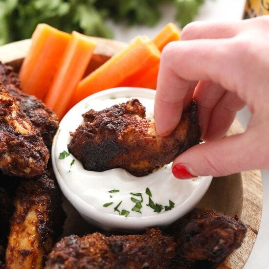 A person enjoying dry rub wings by dipping them into a bowl of dip.