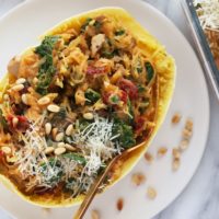 Instant Pot spaghetti squash boats with spinach and pine nuts on a white plate.
