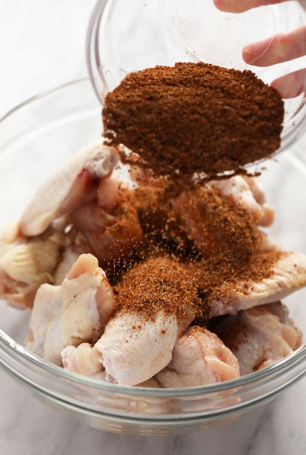 Pouring dry rub over chicken wings 