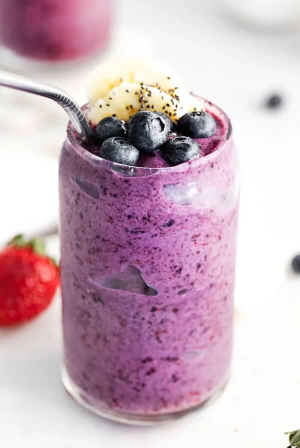 a triple berry smoothie in a glass with a spoon.