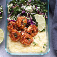 Cajun Shrimp and Grits served in a clear container with lime wedges.