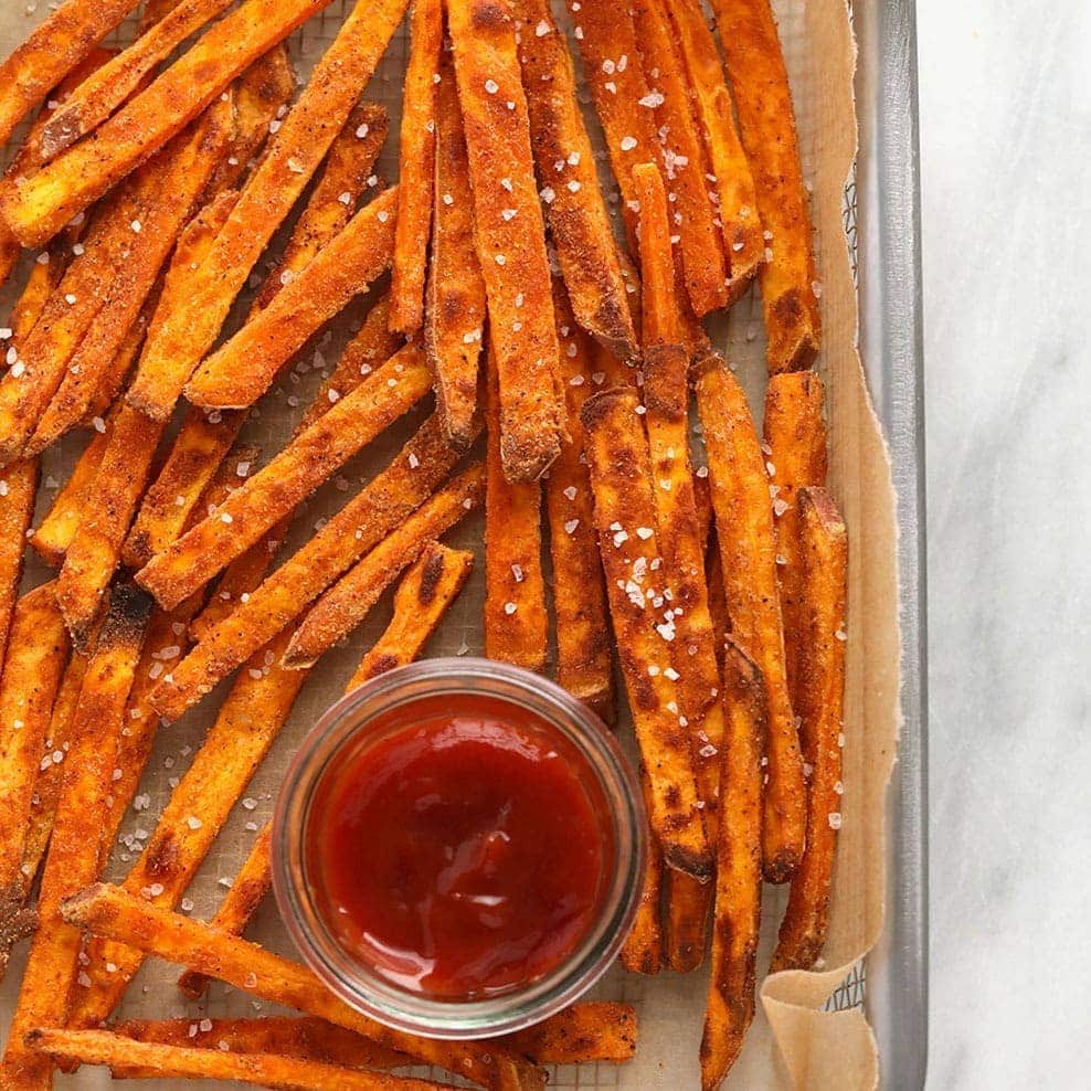Baked sweet potato fries on a baking sheet with ketchup.