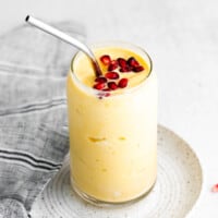 Mango smoothie in a glass with pomegranate seeds on top.
