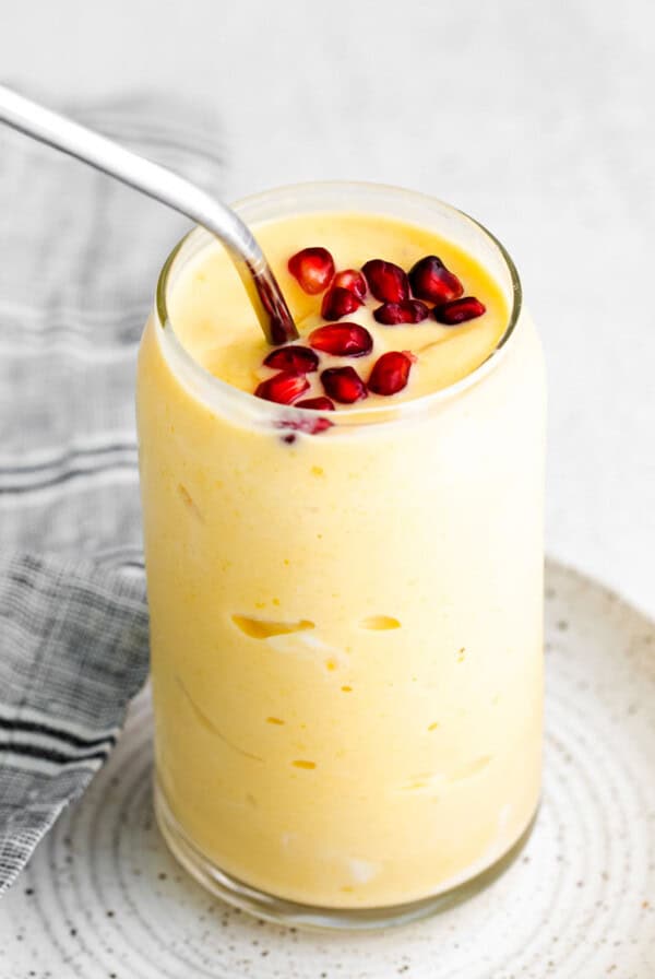 Mango smoothie in a glass with pomegranate seeds on top.