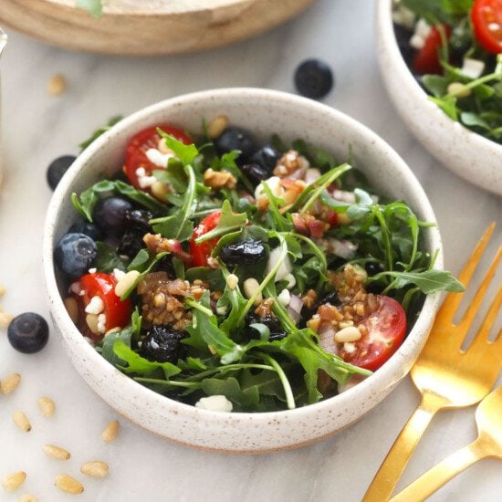 Two bowls of arugula salad with blueberries and walnuts.