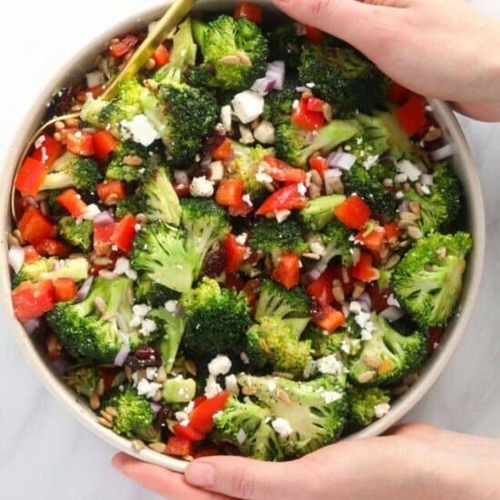 two hands holding a bowl of healthy broccoli salad
