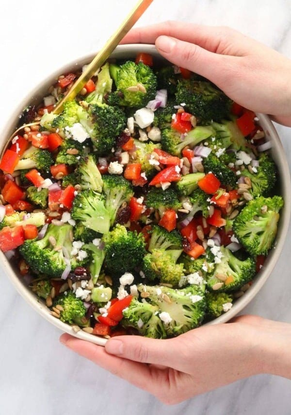 two hands holding a bowl of healthy broccoli salad