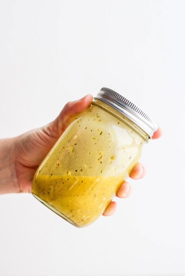 A person holding a mason jar filled with homemade Greek salad dressing.