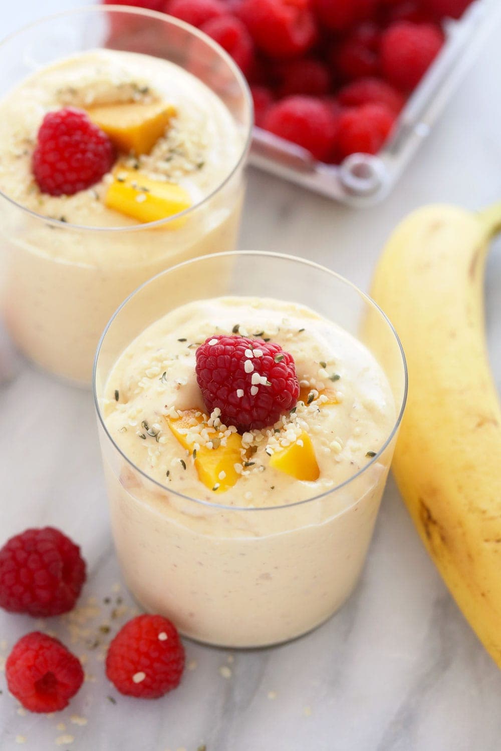 mango smoothie in a glass topped with a raspberry and sliced mango