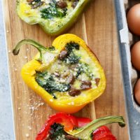 Cheesy breakfast sausage stuffed peppers with spinach and eggs on a cutting board.