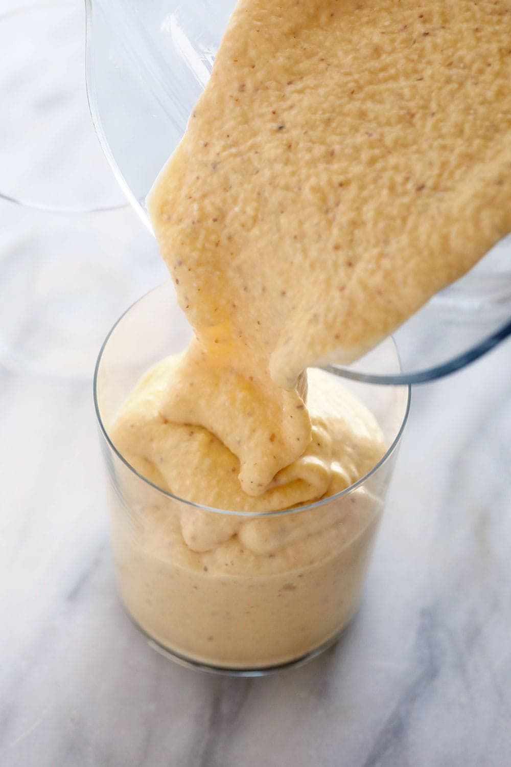 mango smoothie being poured from a blender into a glass