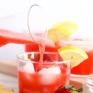 A glass of strawberry lemonade infused with a splash of strawberry vodka being poured into a glass.