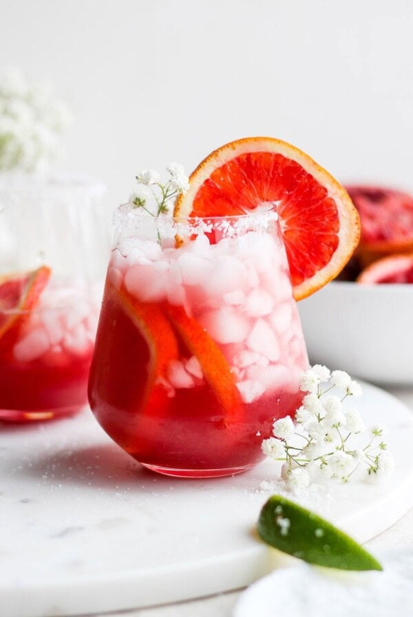 two glasses of blood orange margarita with ice and flowers.