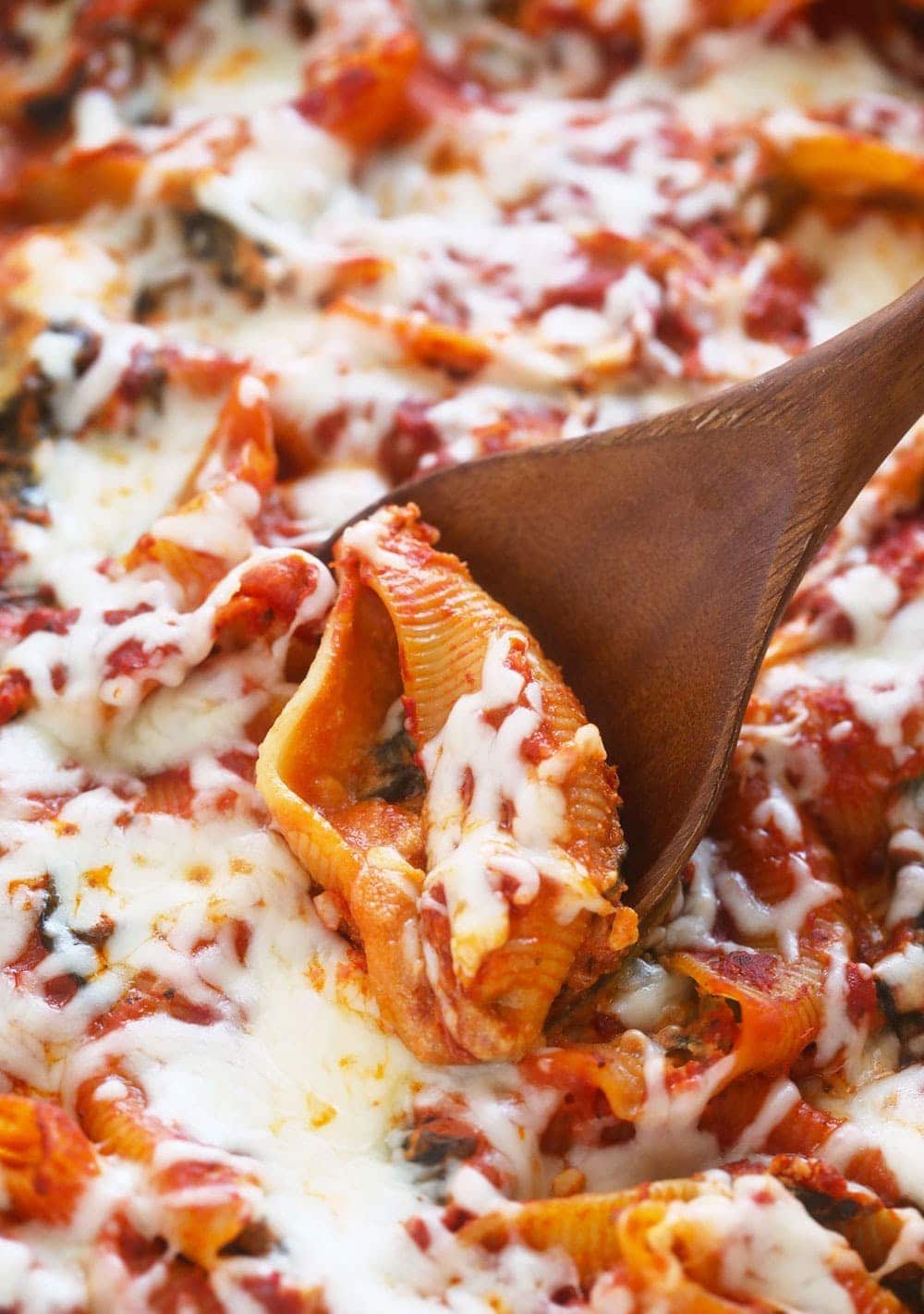 a wooden spoon is being used to scoop out a dish of Stuffed Shells.