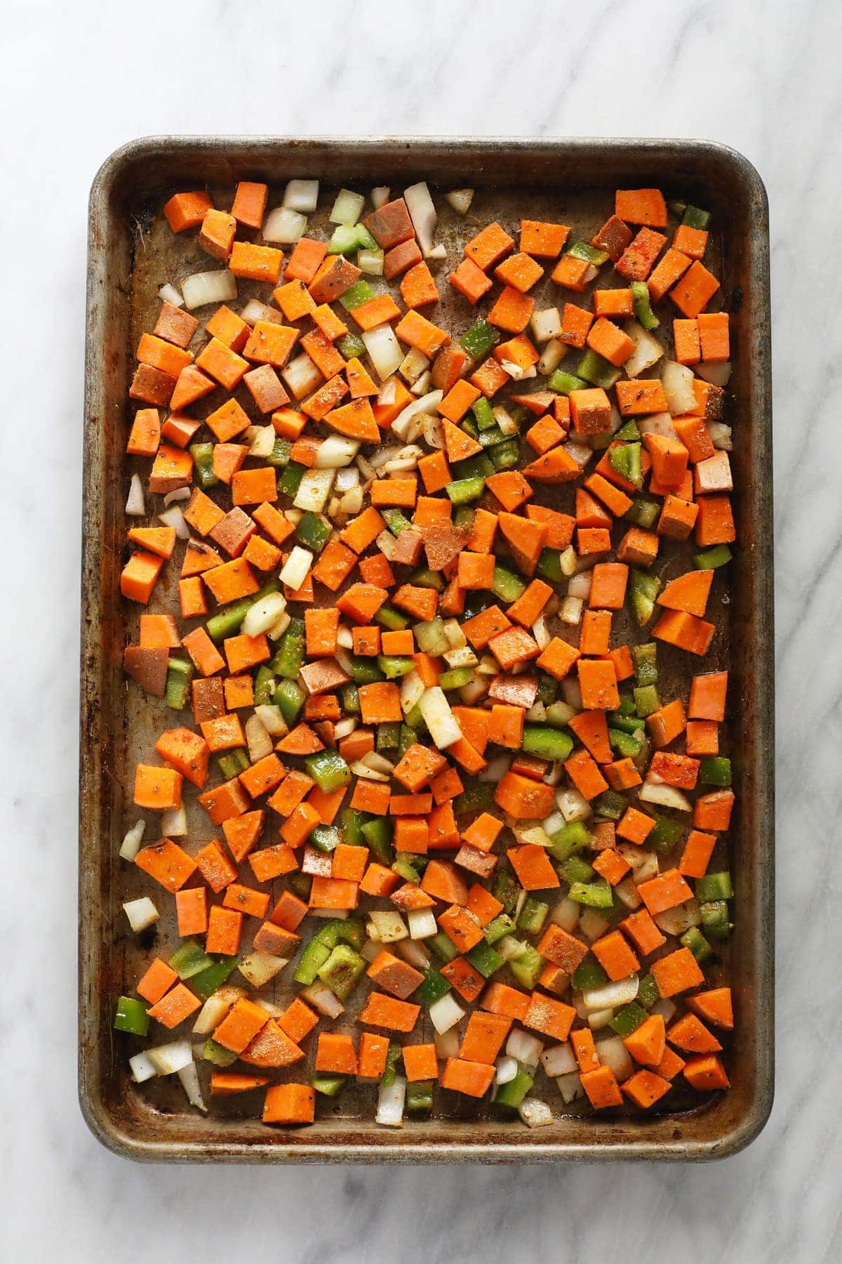 raw sweet potato, bell pepper, and onion on pan.