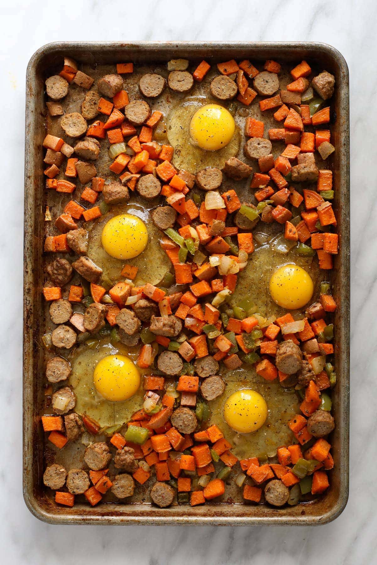 sweet potato nests with raw eggs cracked into them on sheet pan.
