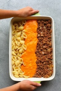 A person holding a hamburger casserole dish with the ingredients before they're mixed together.