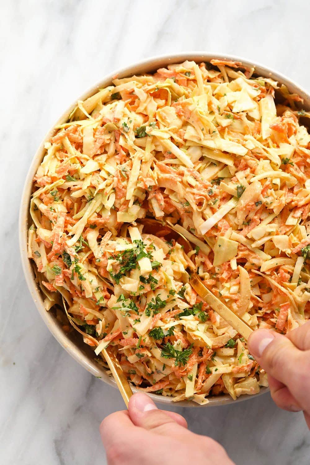 creamy coleslaw in a bowl being served with serving spoons