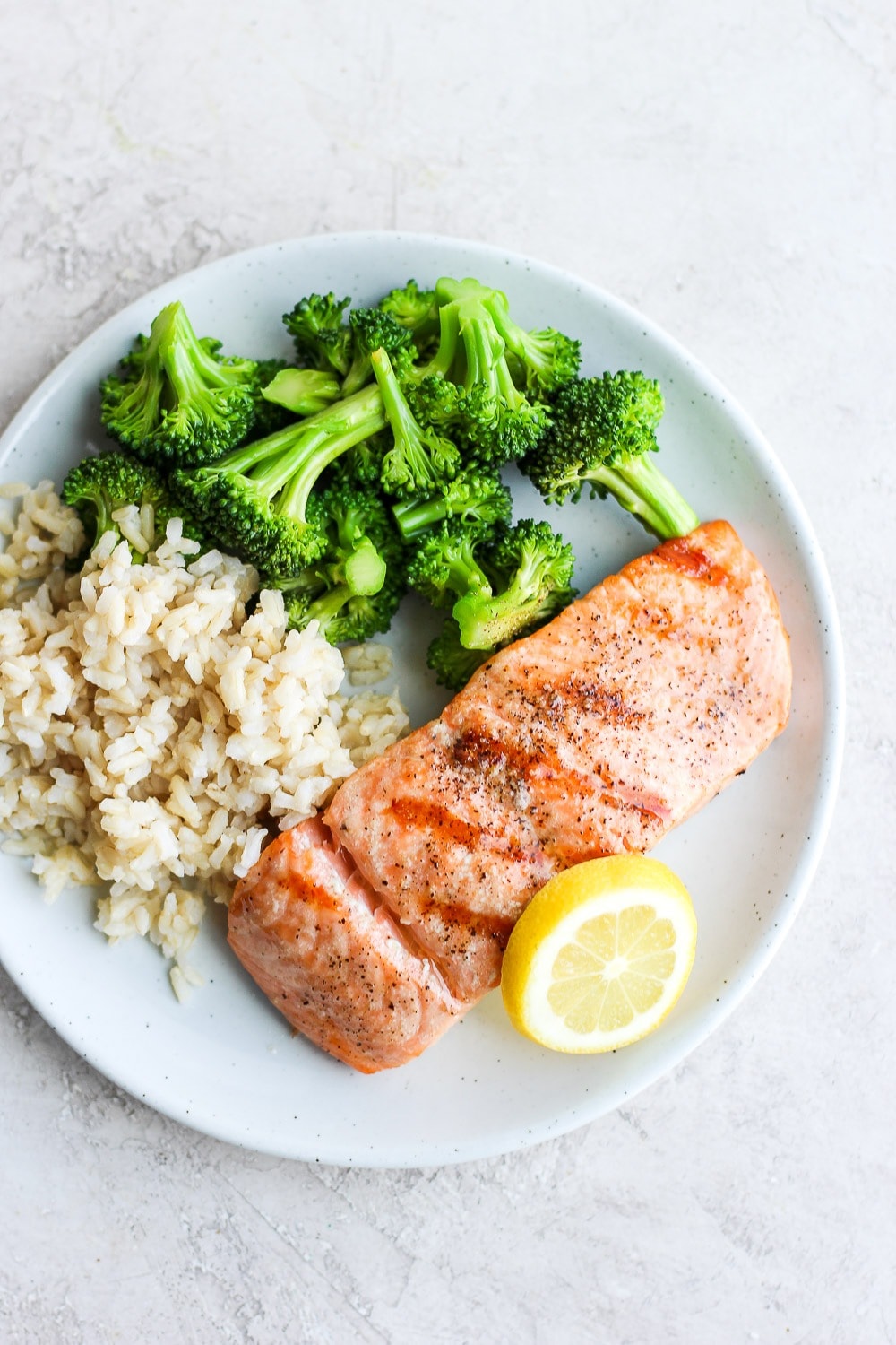 This is grilled salmon on a plate with broccoli and rice. 