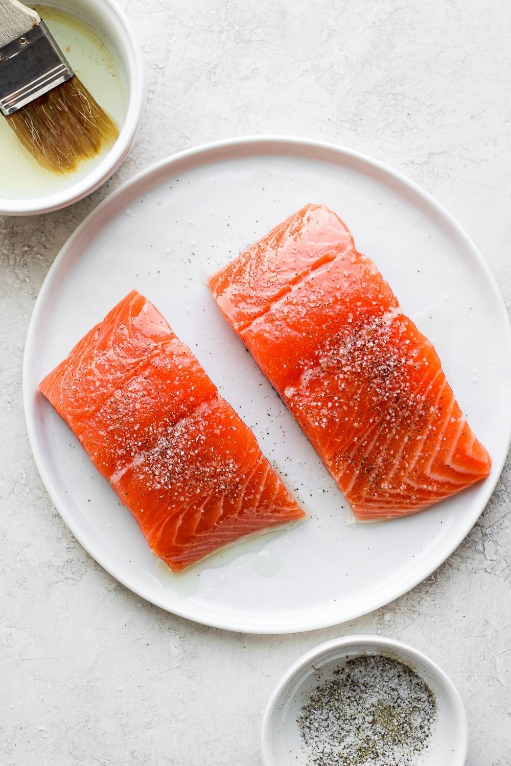 raw salmon filets being brushed with olive oil