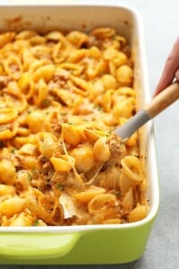 A person scooping hamburger pasta out of a casserole dish.