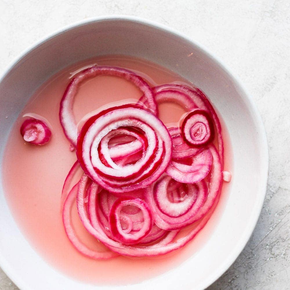 Quick pickled red onions in a white bowl.