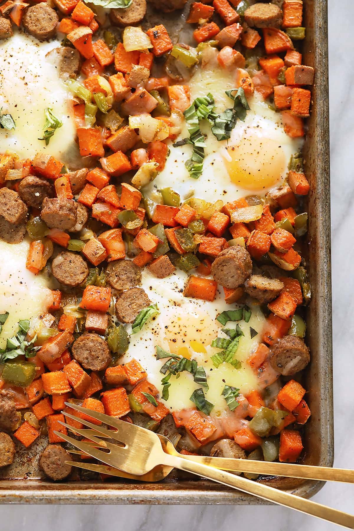sweet potato hash on baking sheet with eggs and 2 forks.