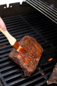 Brushing barbecue sauce onto sous vide ribs on a barbecue grill.